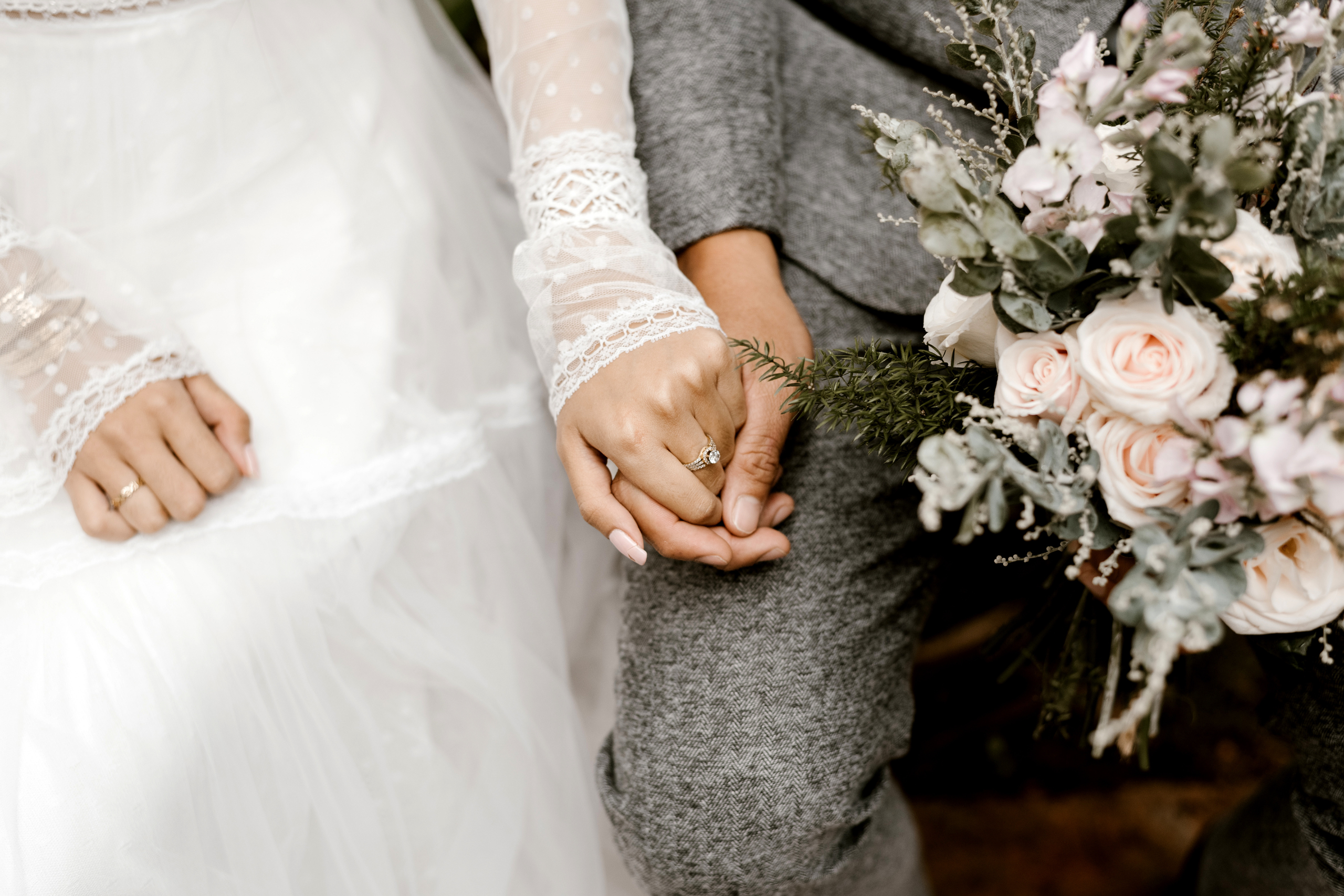 in-boda-classic-fotografia-manos-de-pareja-con-anillo-vestido-blanco-traje-gris-con-ramo.jpg