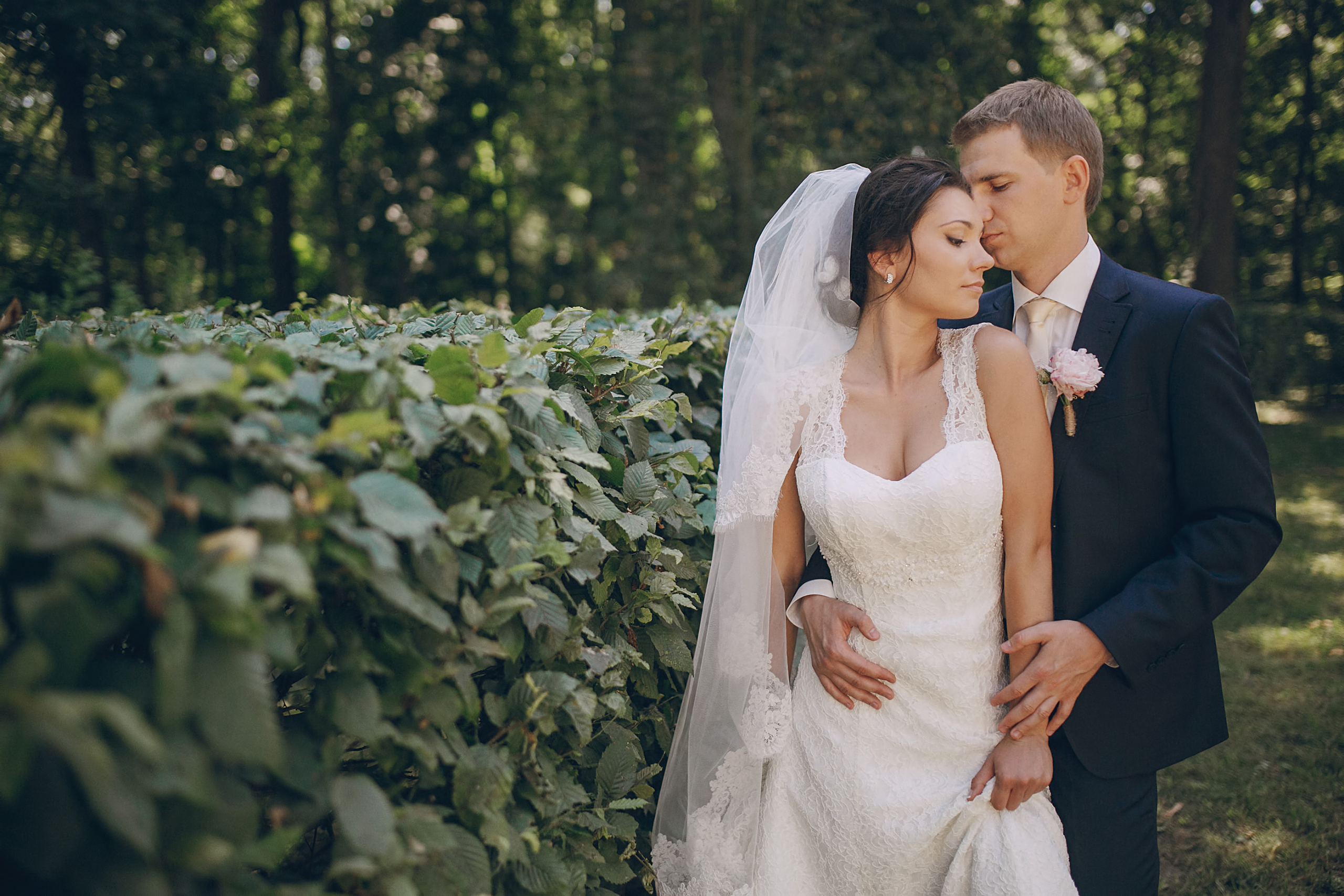 in-boda-classic-fotografia-pareja-abrazada-en-jardin-hombre-detras-vestido-blanco-traje-azul.jpg