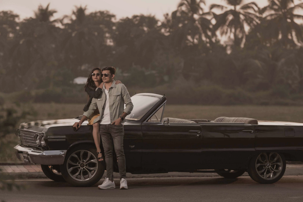 in-boda-elegant-style-fotografia-pareja-hombre-de-pie-mujer-sentada-en-capo-vehiculo-negro-descapotable.jpg